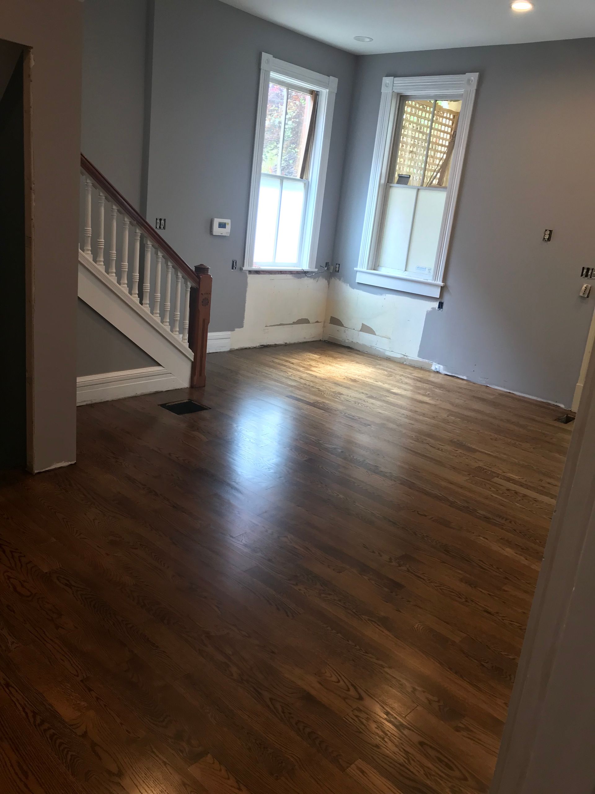 An interior room with hardwood floors, gray walls, a wooden staircase, and two white-framed windows under construction.