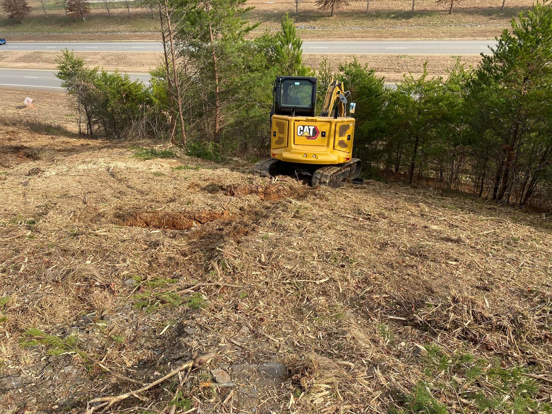 A yellow excavator is working in a field next to a road.