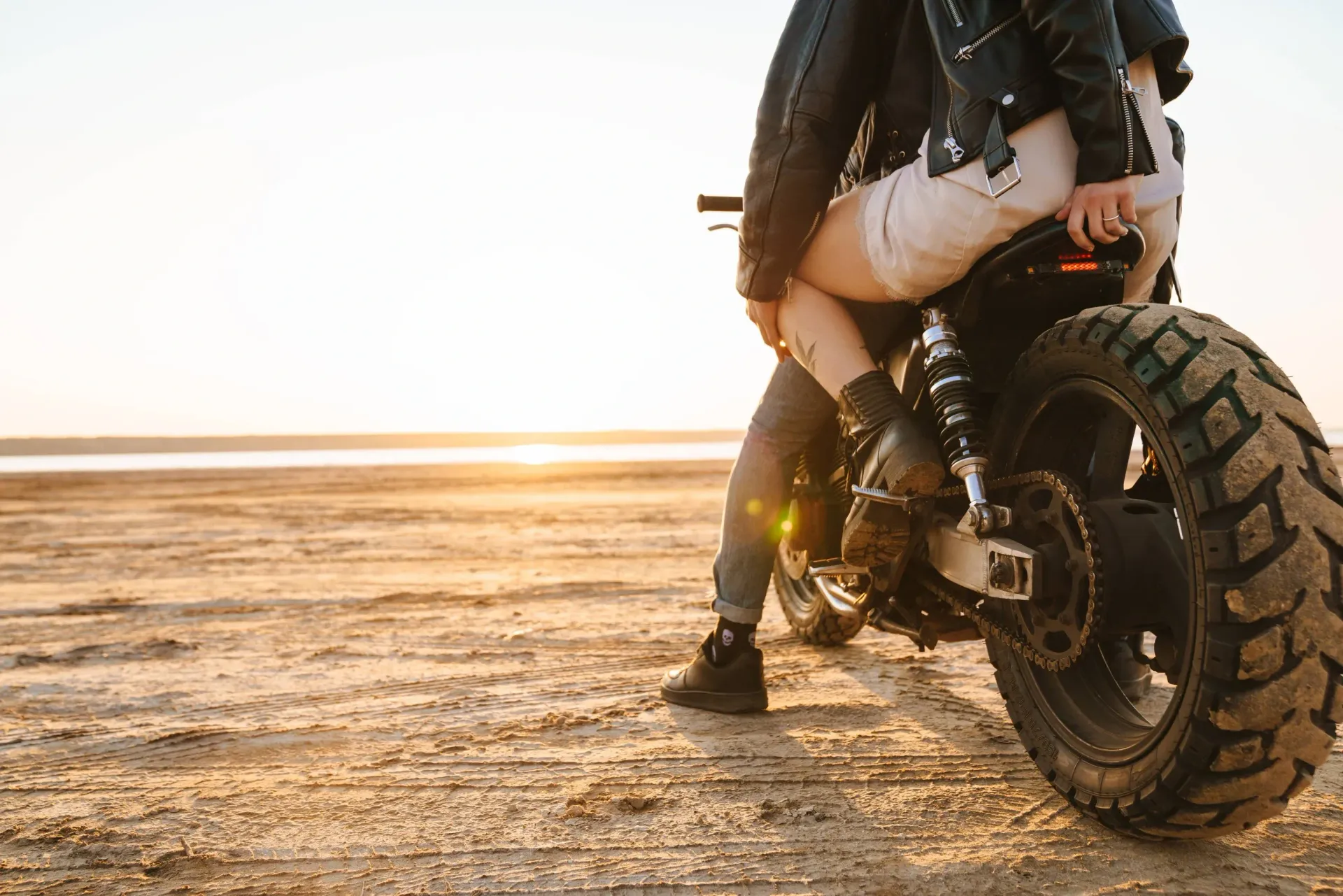 Couple sitting on a motorcycle on the beach enjoying the sunset.