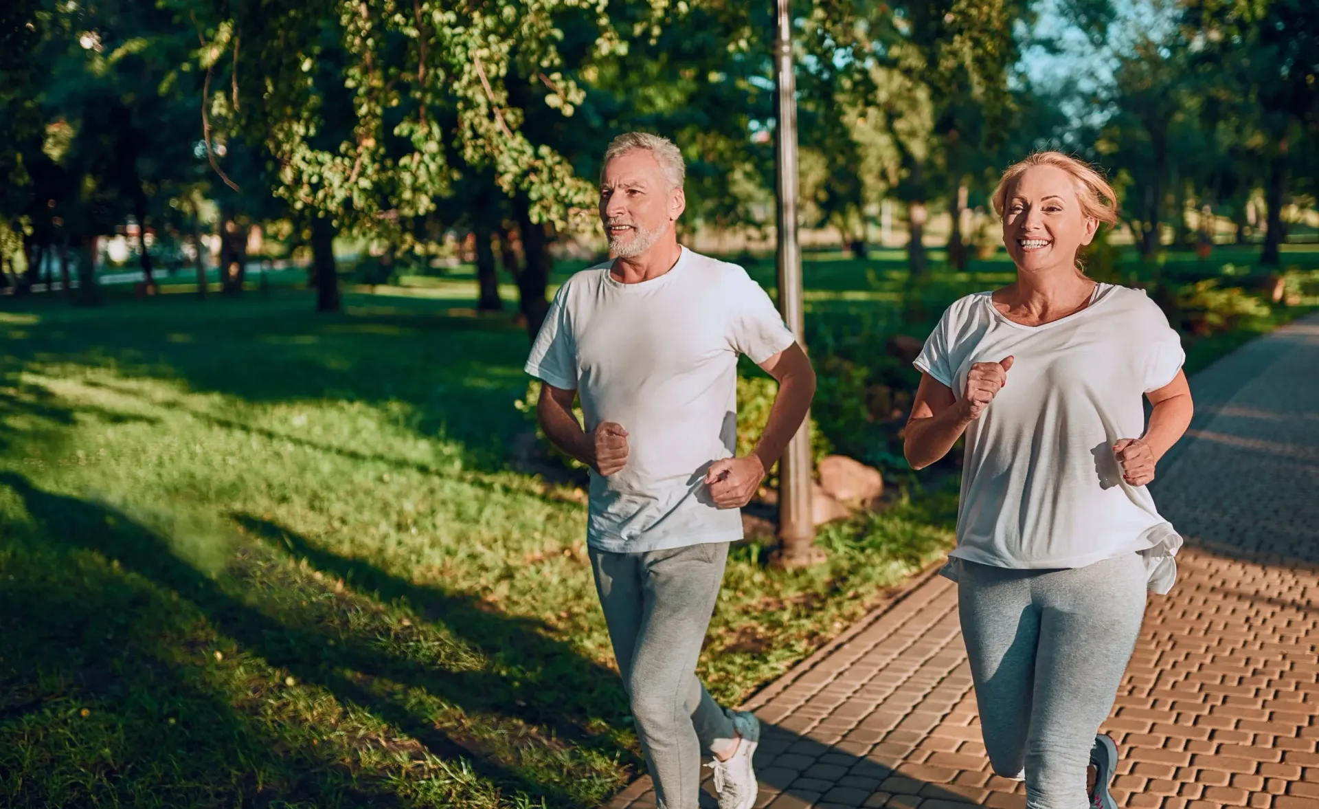 Two adults jogging along a tree-lined park path.