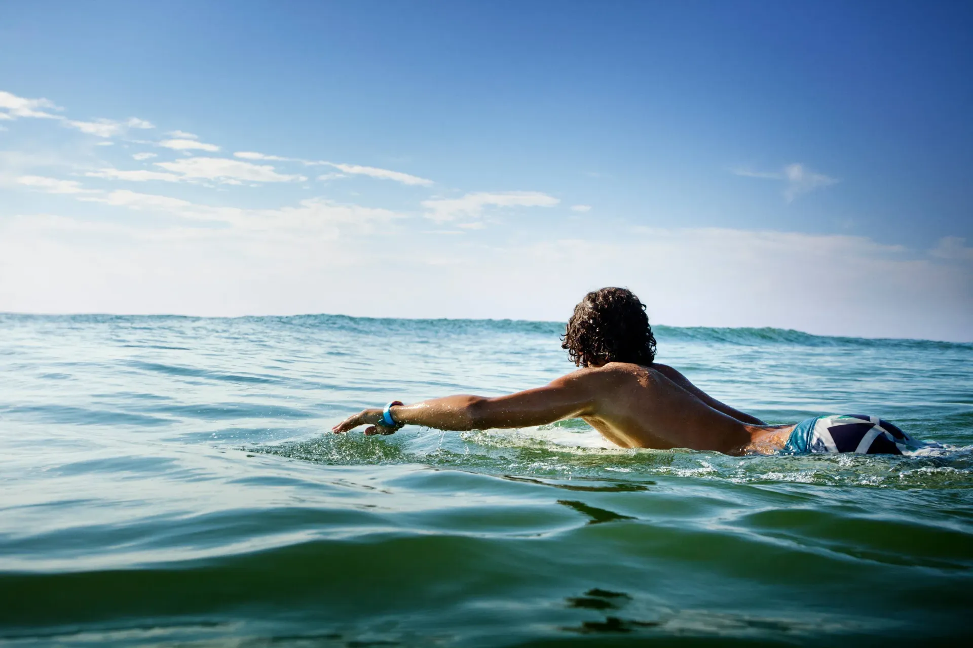 Man swimming in ocean, blue sky overhead.