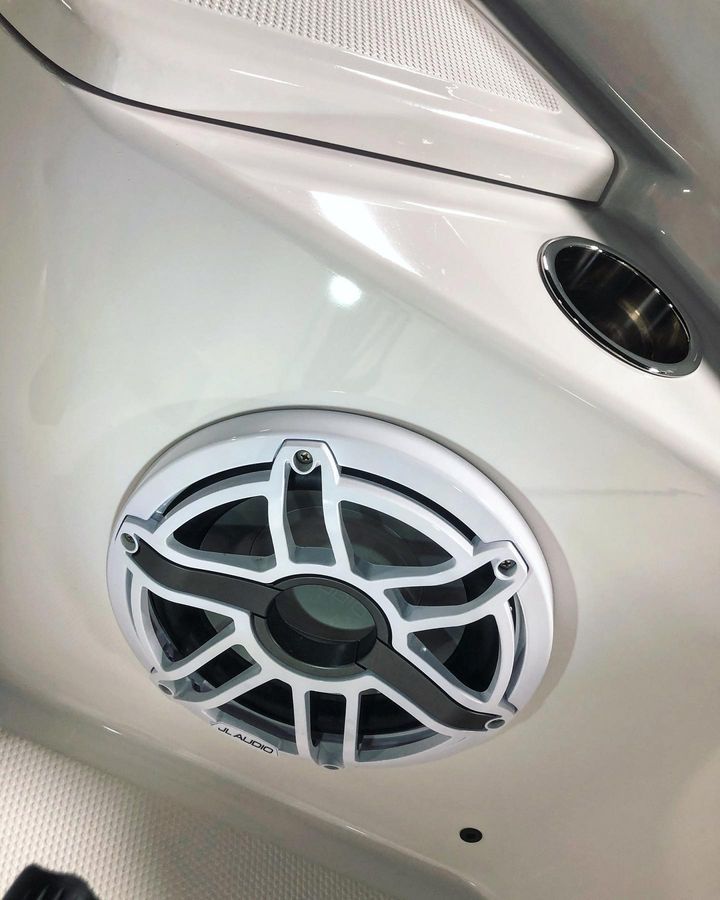 White boat speaker with silver grill, mounted on a white wall, next to a cup holder.