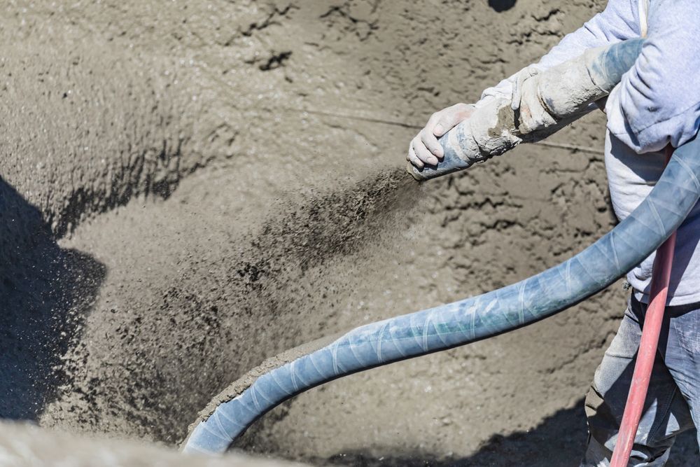 Person Spraying Cement Into a Hole With a Blue Hose; Construction Site — Atherton Tableland Concreting in Tolga, QLD
