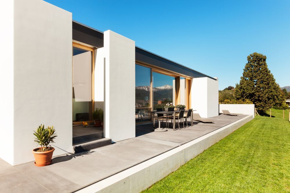 Modern White House With Large Windows, Patio Furniture, and a Green Lawn — Atherton Tableland Concreting in Yungaburra, QLD
