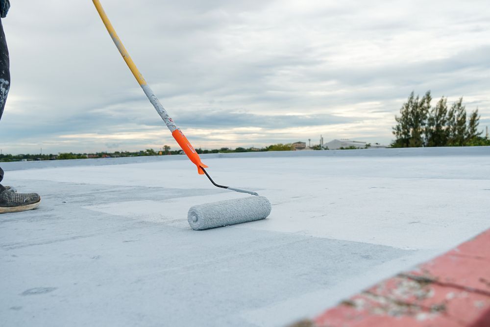 Person Painting a Flat, White Roof With a Roller — Atherton Tableland Concreting in Yungaburra, QLD