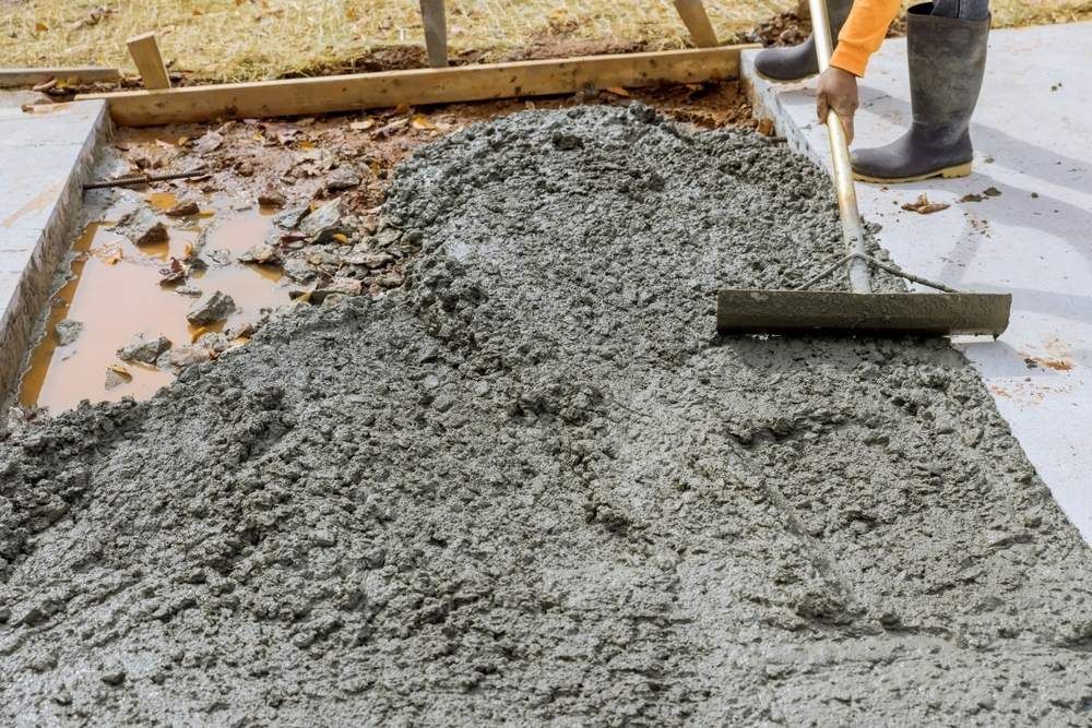 A Man is Spreading Concrete on a Sidewalk With a Rake — Atherton Tableland Concreting in Mareeba, QLD