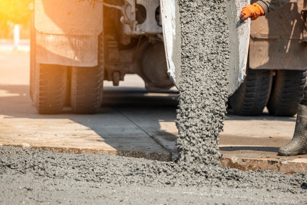 A Man Is Pouring Concrete From A Truck Onto A Sidewalk — Atherton Tableland Concreting in Mareeba, QLD