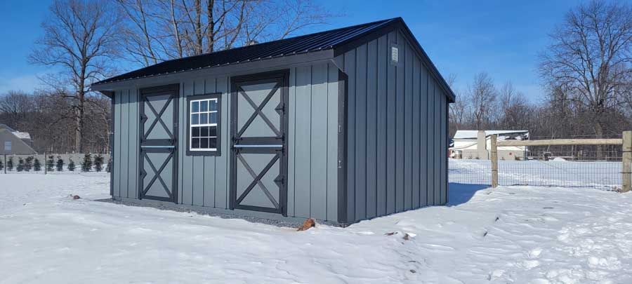 A grey metal shed with two dark-trimmed doors and a central window, set in a snowy field under a clear blue sky.