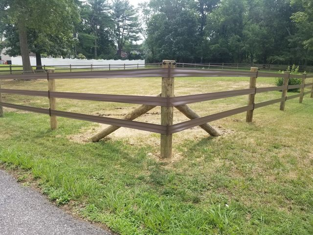 A three-rail wooden fence forms a corner in a grassy yard, with angled support posts for stability.