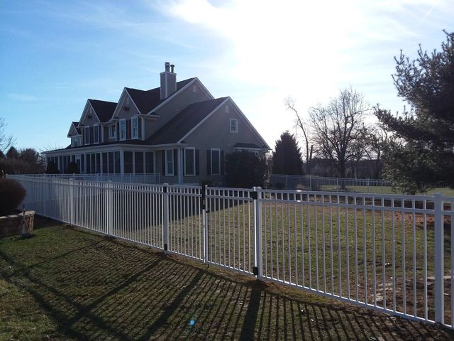A white metal fence runs across the foreground of a grassy yard, with a large suburban house in the background.