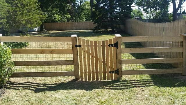 A wooden split-rail fence with wire mesh and a central arched gate in a grassy backyard.