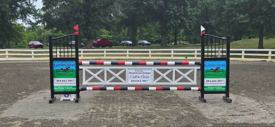 A show jumping fence with black and white standards, red, black, and white rails, and central sponsor signage.