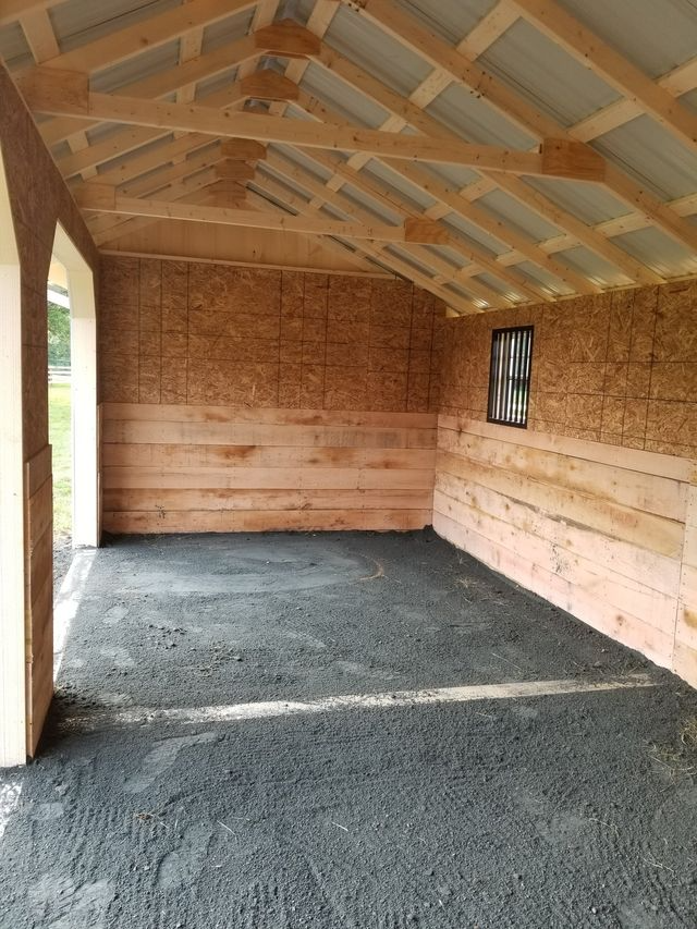 Interior of a shed with wood walls, exposed rafters, a dirt floor, and a small square window on the right wall.