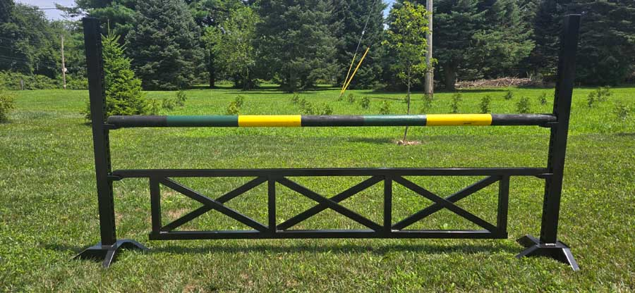 A horse jumping rail obstacle with a green and yellow striped pole set on black stands in a grassy field.