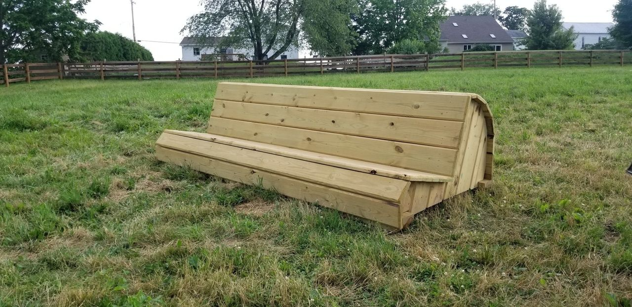 A wooden cross-country equestrian jump shaped like a wedge sitting in a grassy field.