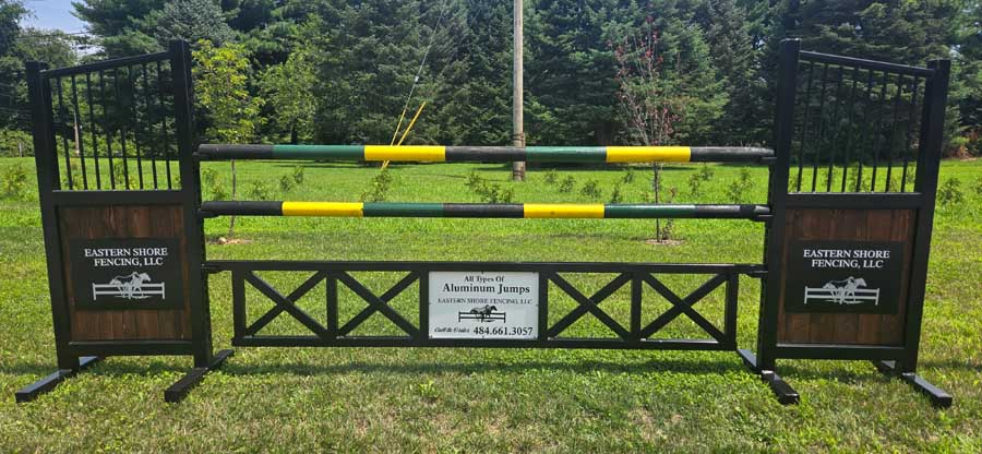 A horse jumping obstacle with wooden side panels and two horizontal rails striped in green and yellow in a grassy field.