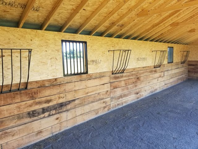 A stable interior featuring wooden walls, grated windows, and metal hay racks mounted along the side.