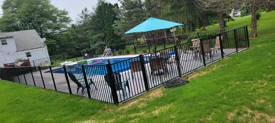 A backyard swimming pool covered by a blue tarp, surrounded by a black metal fence with patio furniture and an umbrella.