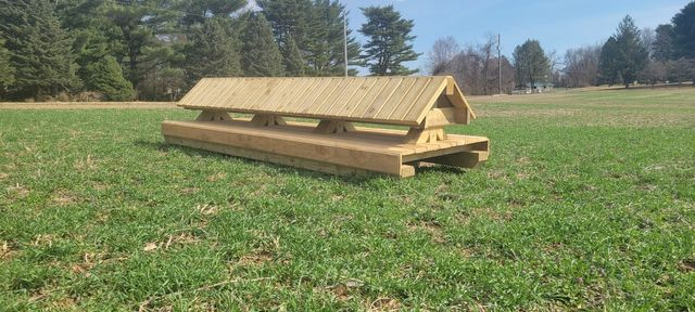 A wooden portable cross-country jump obstacle sits in the center of a grassy field on a sunny day.