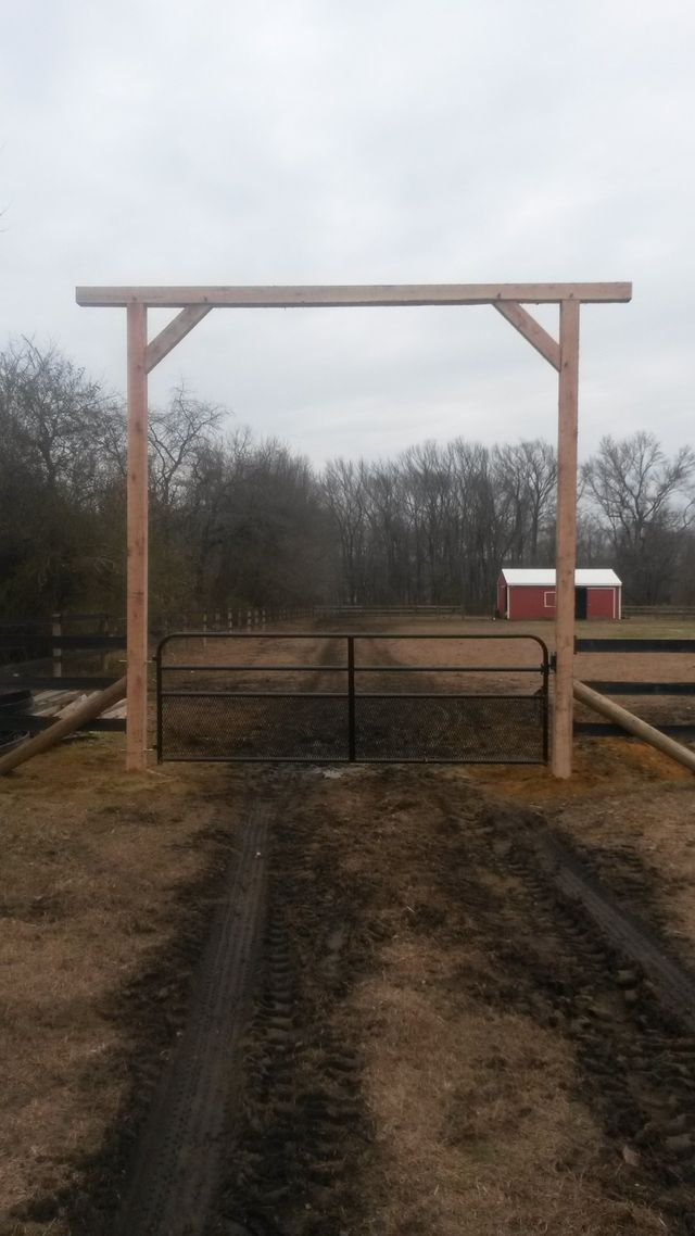 A metal gate set between two tall wooden posts in a field, with a red barn visible in the distance.