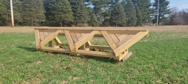 A wooden equestrian cross-country jump obstacle shaped like a geometric triangular trestle, sitting on a grassy field.