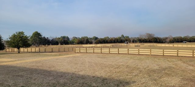 A sprawling, dry grassy pasture enclosed by wooden post-and-rail fencing under a pale blue sky.