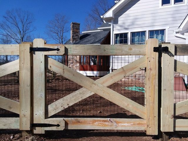 A wooden gate with a cross-brace design and black hinges installed in front of a white house.