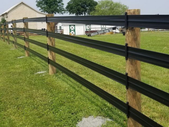 Black, multi-rail flexible fencing attached to wooden posts in a green grassy field.