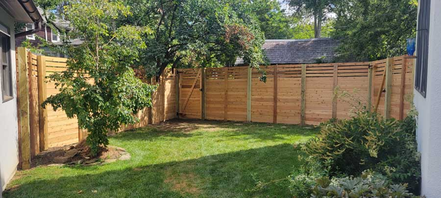 A small green backyard featuring a newly installed wooden fence with horizontal slats and a matching gate.