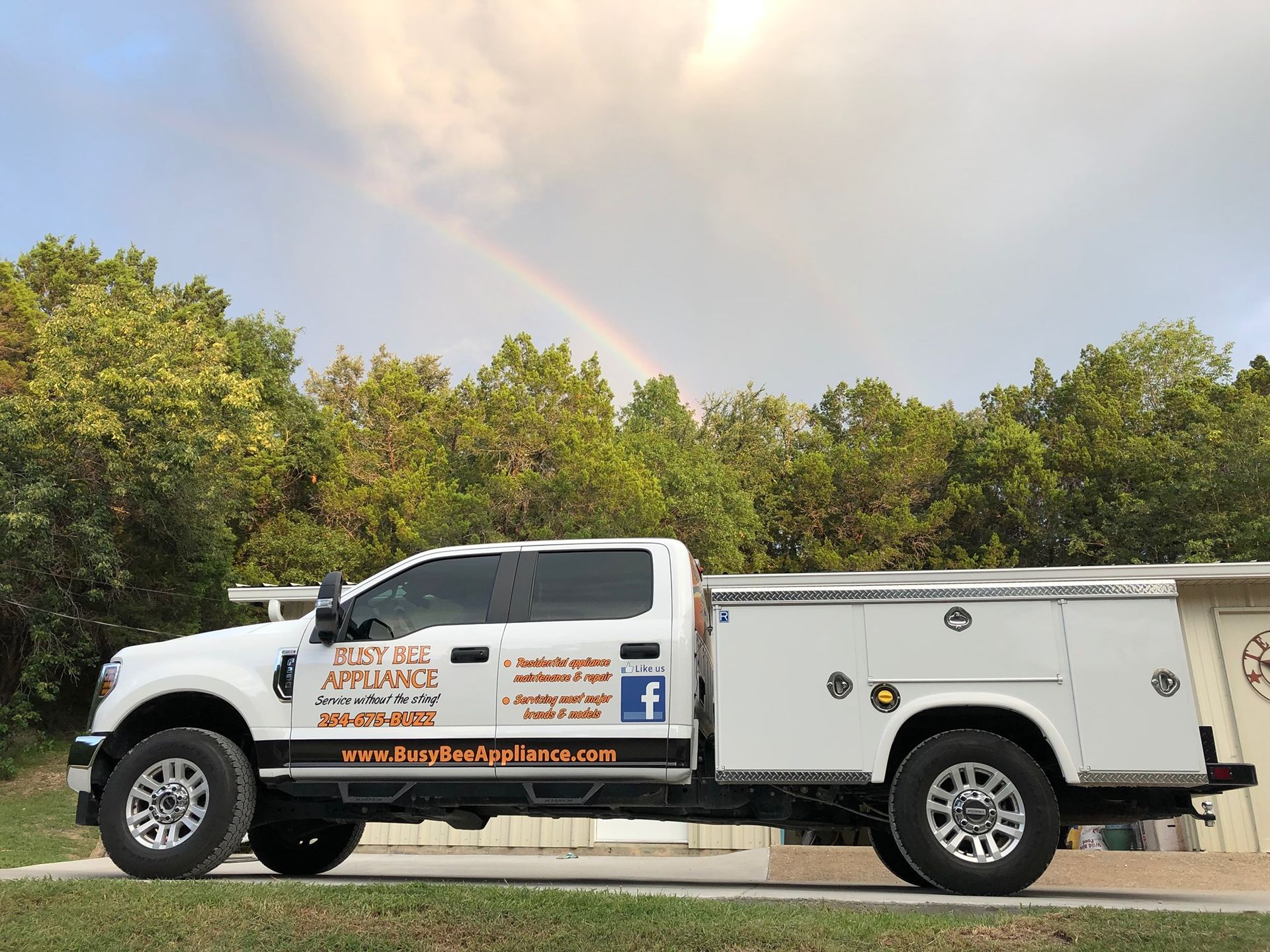 A white truck is parked in front of a house with a rainbow in the sky.