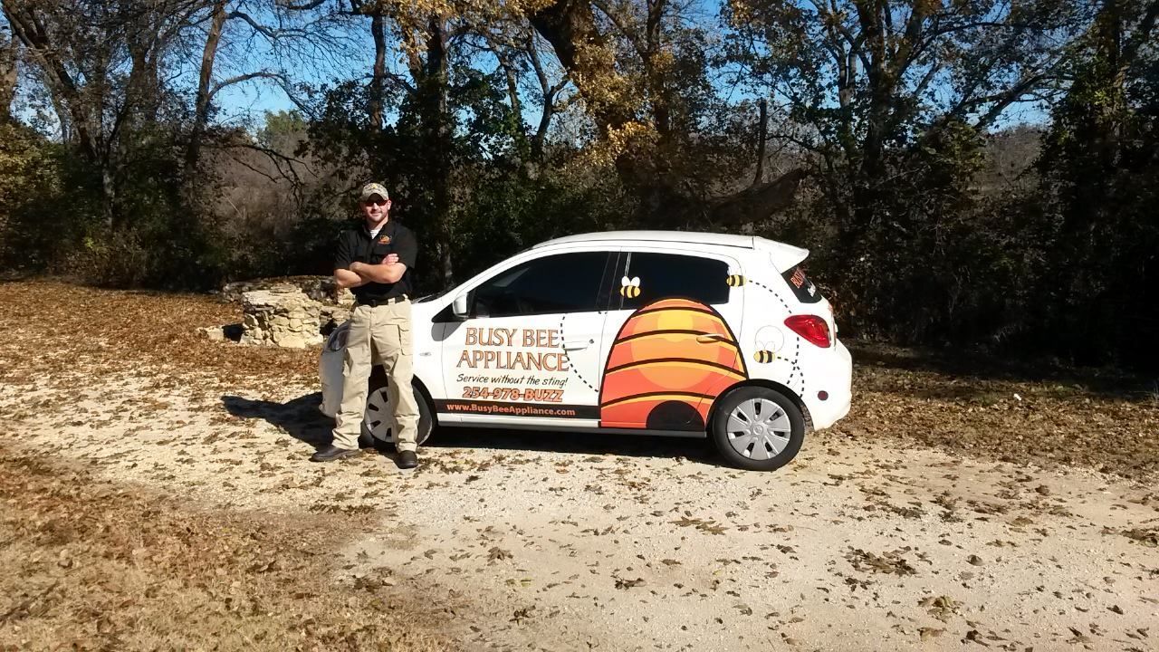 A man is standing next to a white car with a beehive on the side.