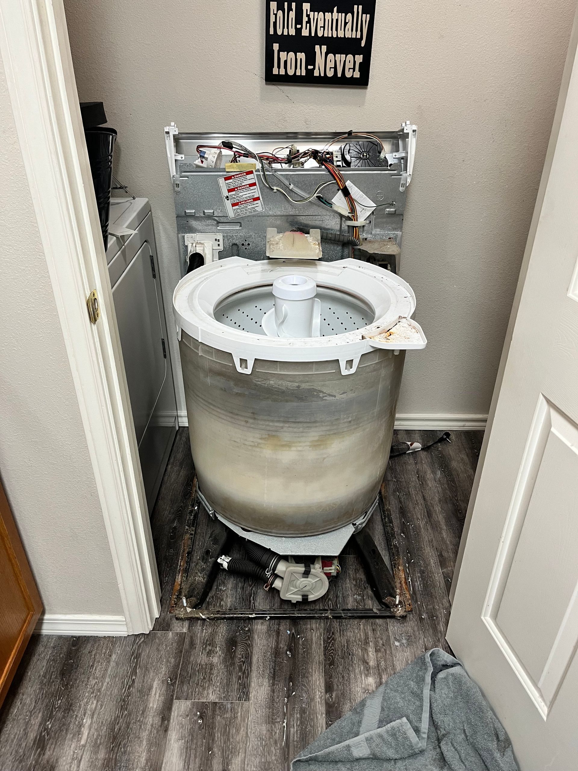 A washing machine is sitting in a laundry room with a sign on the wall above it.