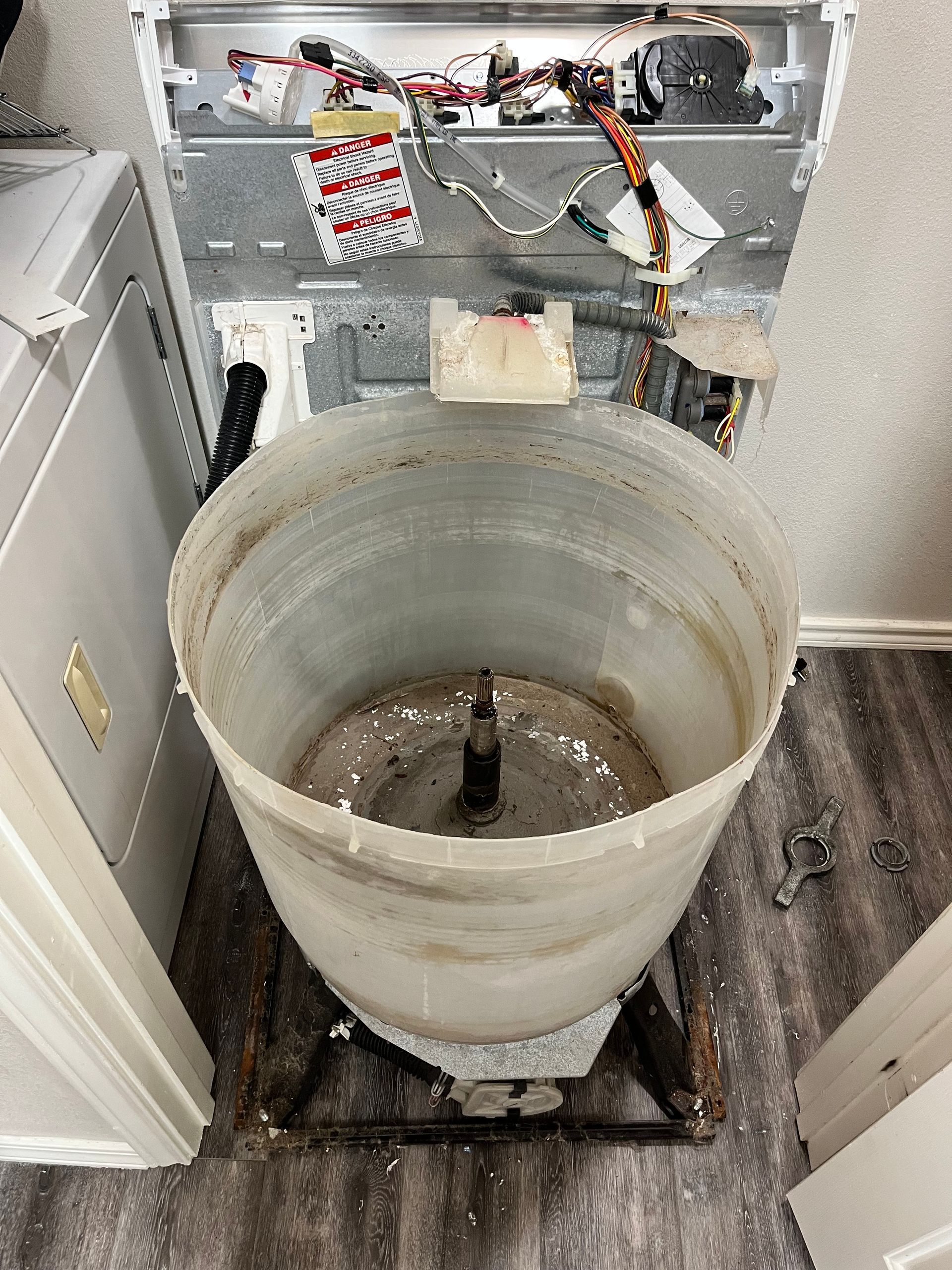 A dirty washing machine is sitting in a laundry room next to a washer and dryer.
