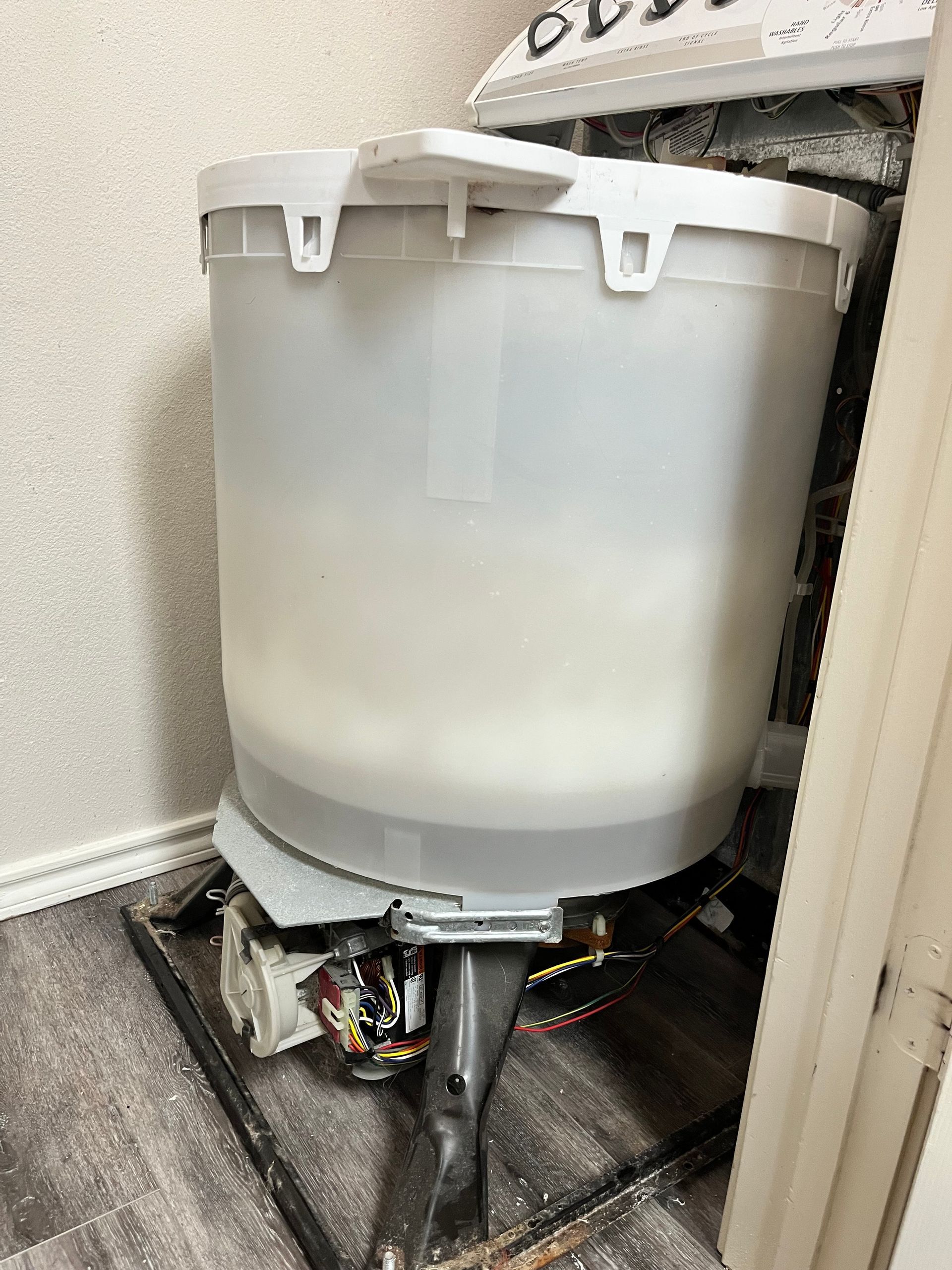 A white bucket is sitting on top of a wooden floor next to a door.