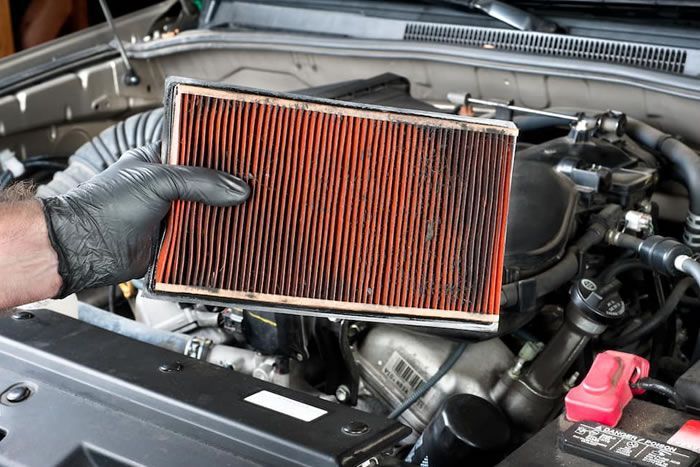 Gloved hand holding a car engine air filter beside the open hood