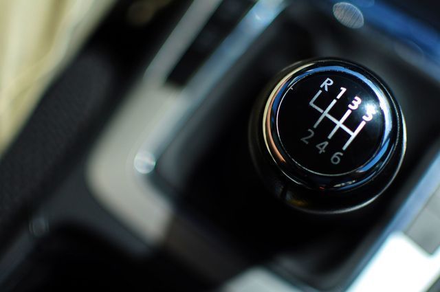 Close-up of a manual car gear shift knob with white shift pattern in a dark interior