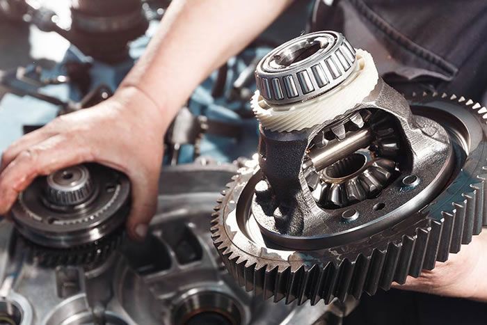 Hands repairing exposed metal gears in a mechanical assembly unit