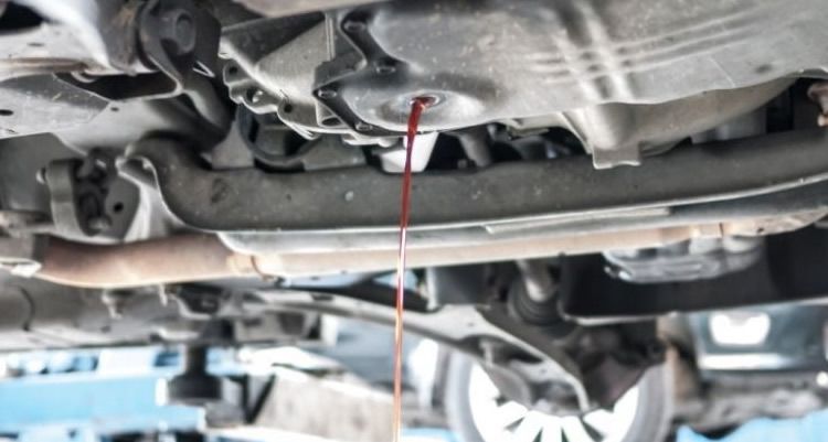 Undercarriage of a car on a lift, with a red inspection line pointing to a metal part below.