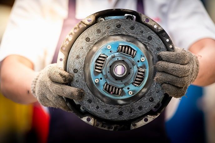 Gloved hands holding a car clutch plate and pressure plate in a workshop