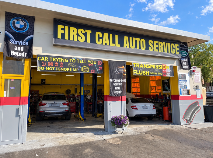Auto service garage storefront with open bays, yellow signage, and cars inside and parked outside | First Call Auto Service