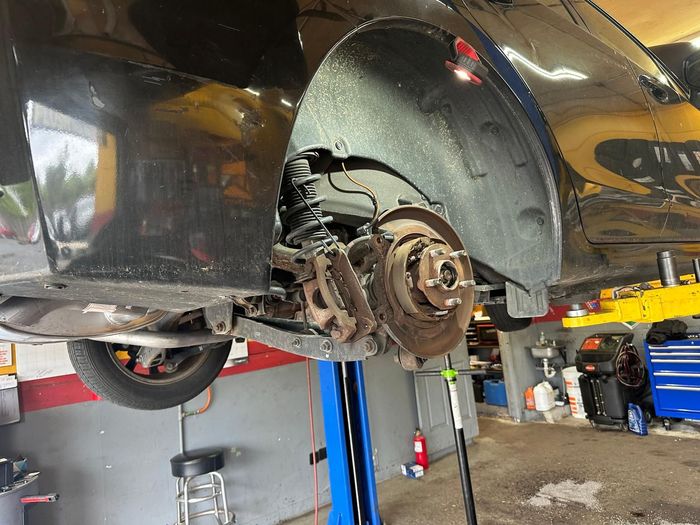 Car raised on a lift, showing a wheel hub and brake assembly in an auto shop | First Call Auto Service