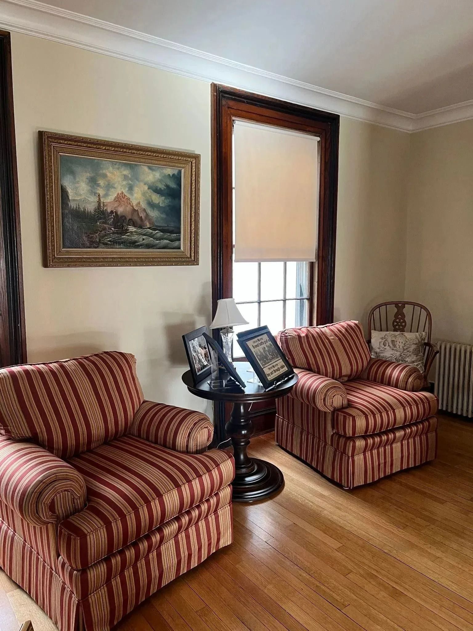 Living room with two striped armchairs, side table, framed art, and a window with a blind