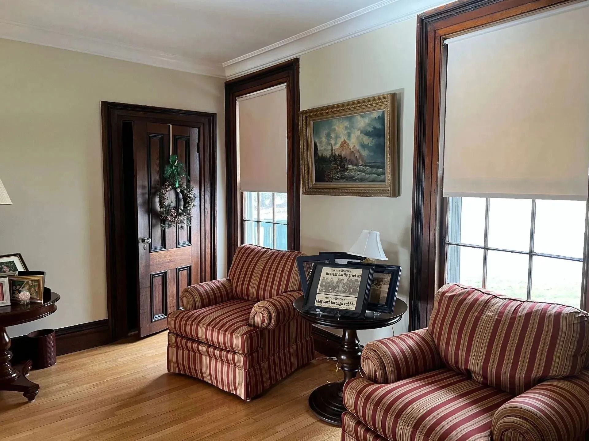 Living room with two striped armchairs, TV stand, wooden door, and framed painting on cream walls.