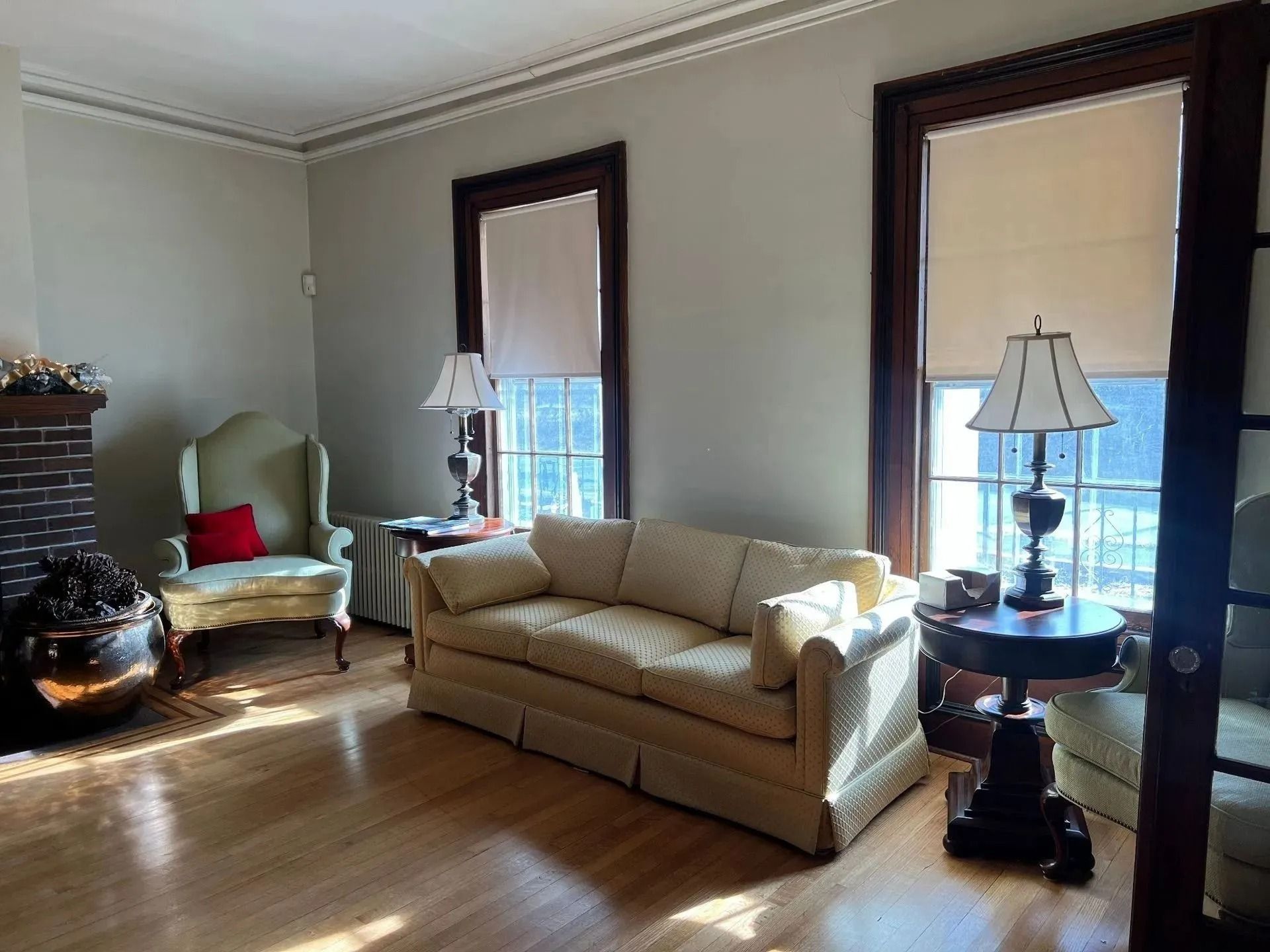 Bright living room with beige sofa, armchair, lamps, and tall windows with blinds.