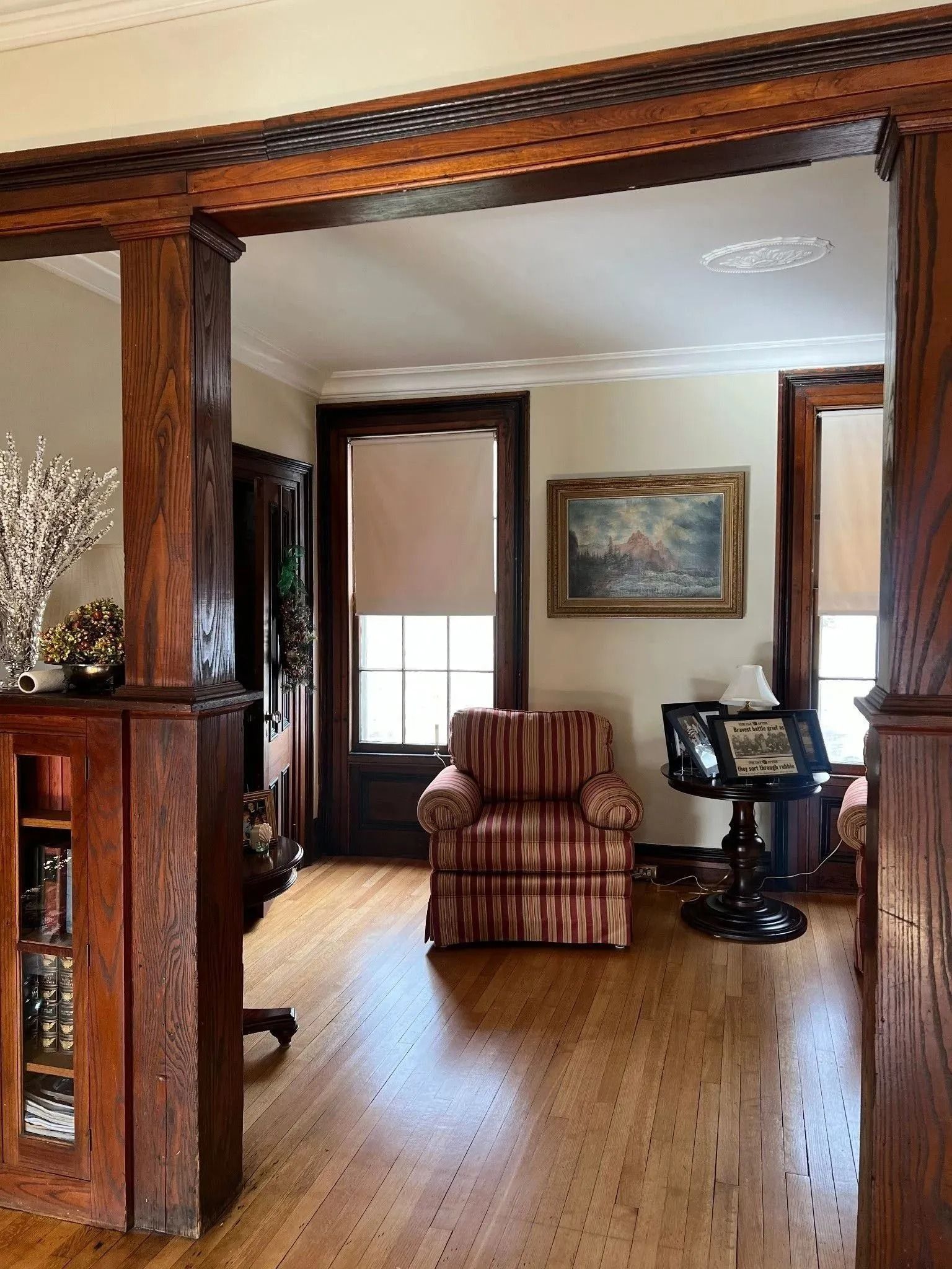 Warm living room with wood floors, striped armchair, framed art, and a small desk by the window.