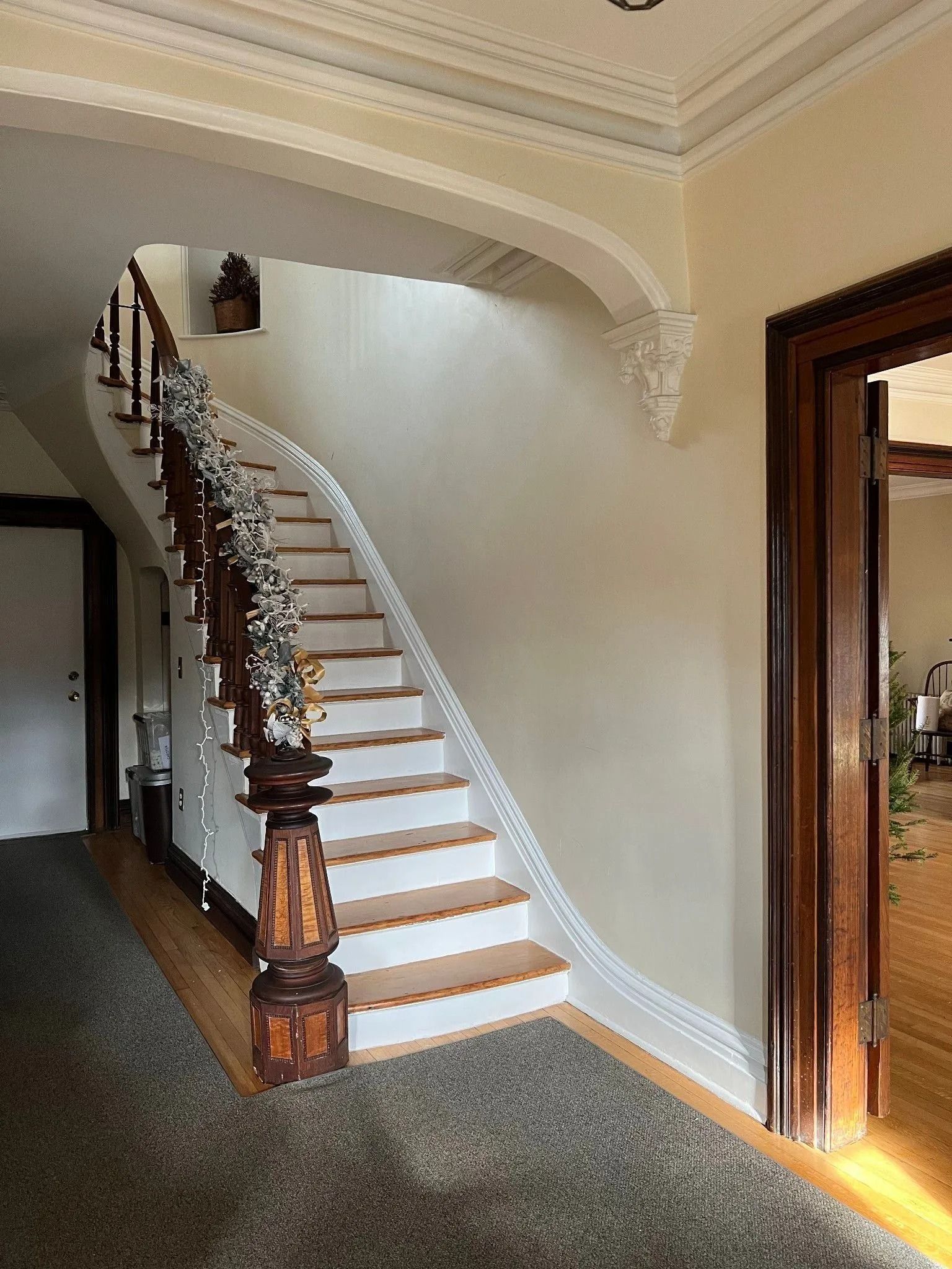 Interior foyer with a carpeted staircase, white walls, and a wooden doorway on the right.