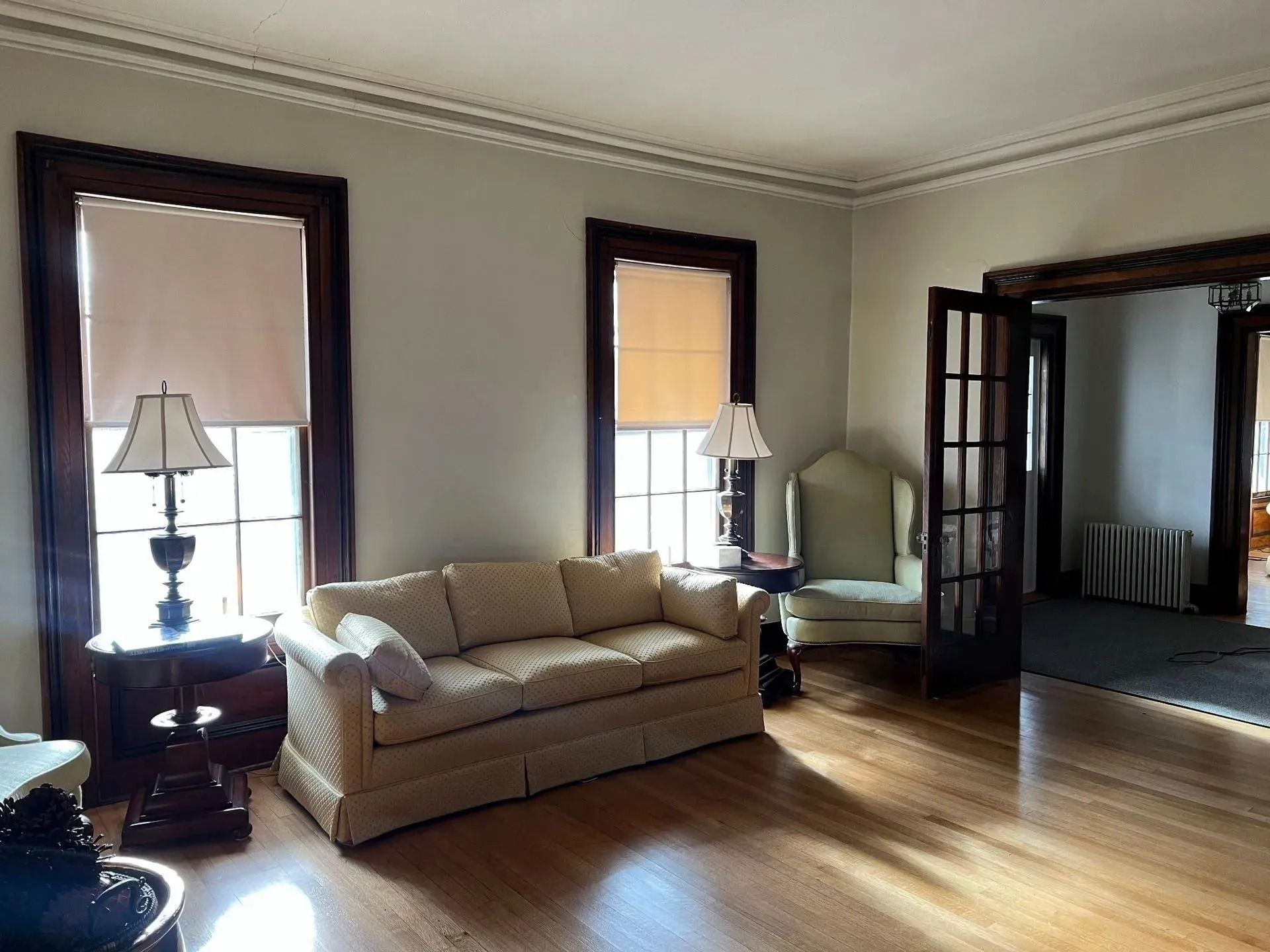 Living room with beige sofa, hardwood floors, tall windows, and French doors leading to another room