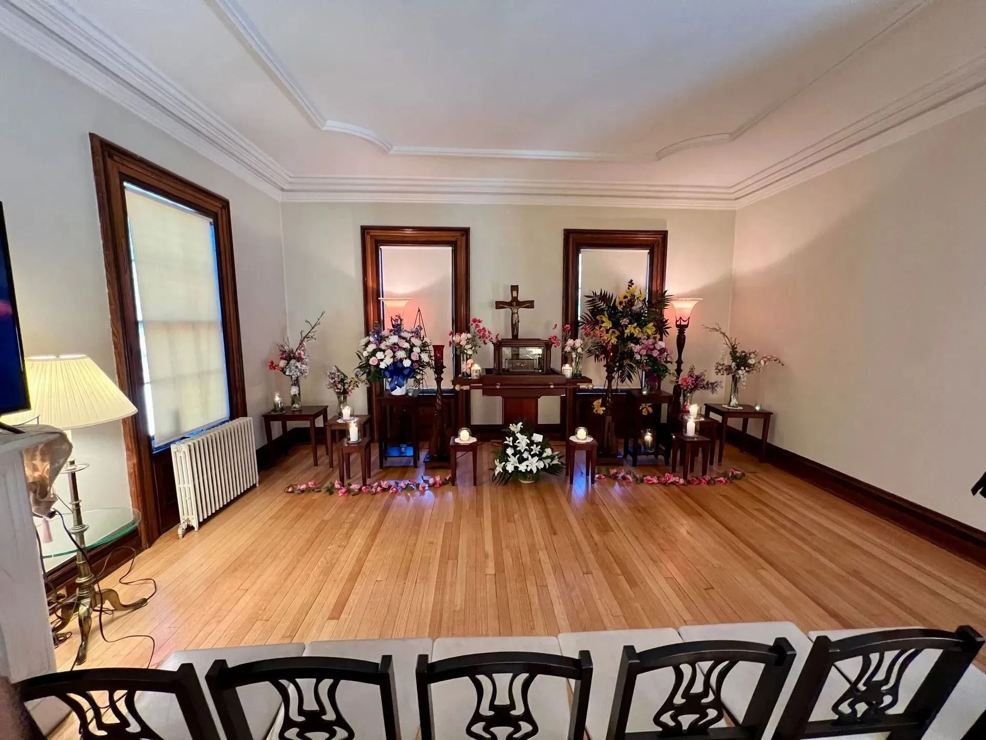 Living room altar with flowers, candles, framed mirrors, and wooden floor in a tidy memorial setting
