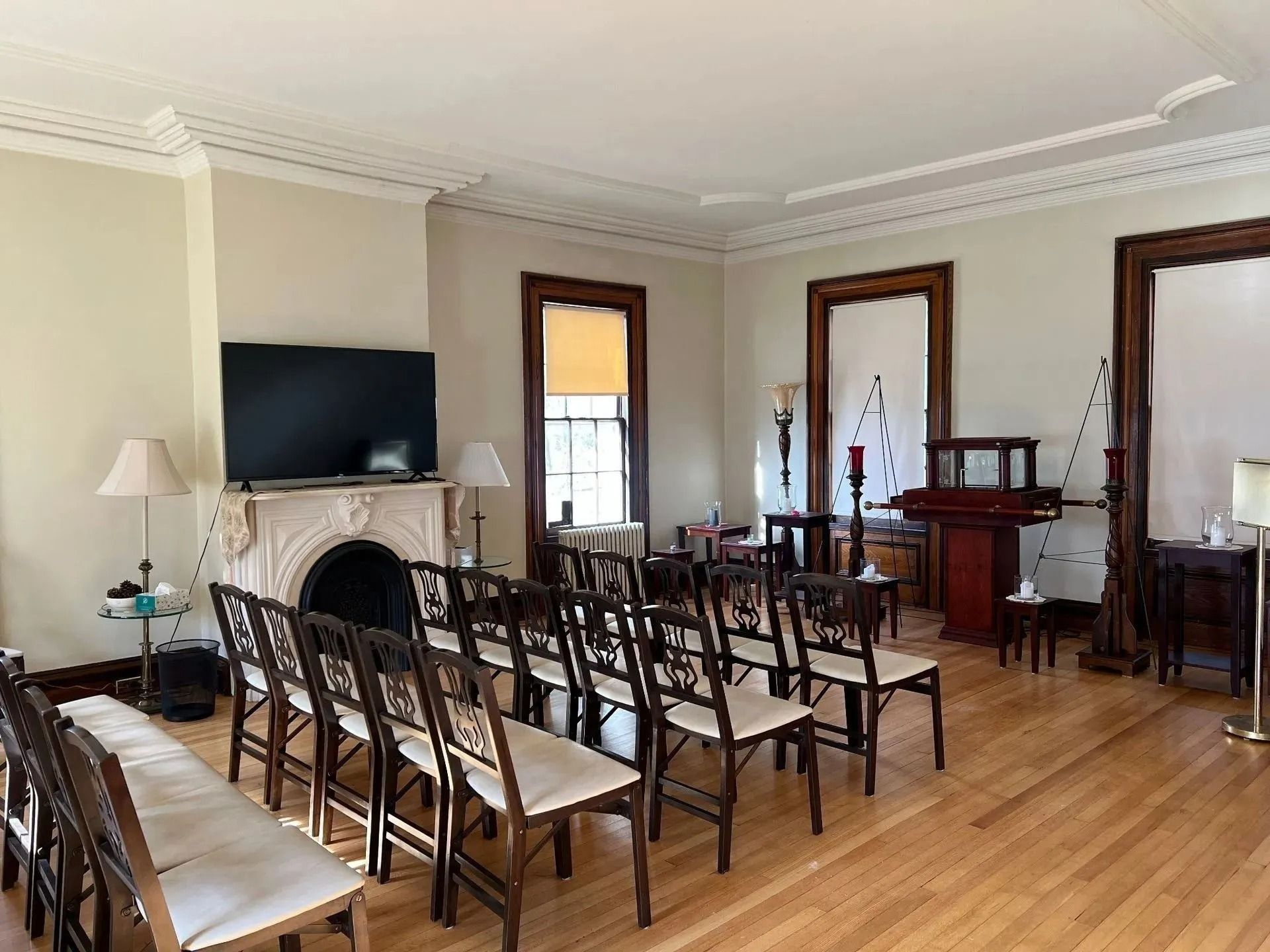 Small meeting room with rows of chairs facing a TV and fireplace on hardwood floors