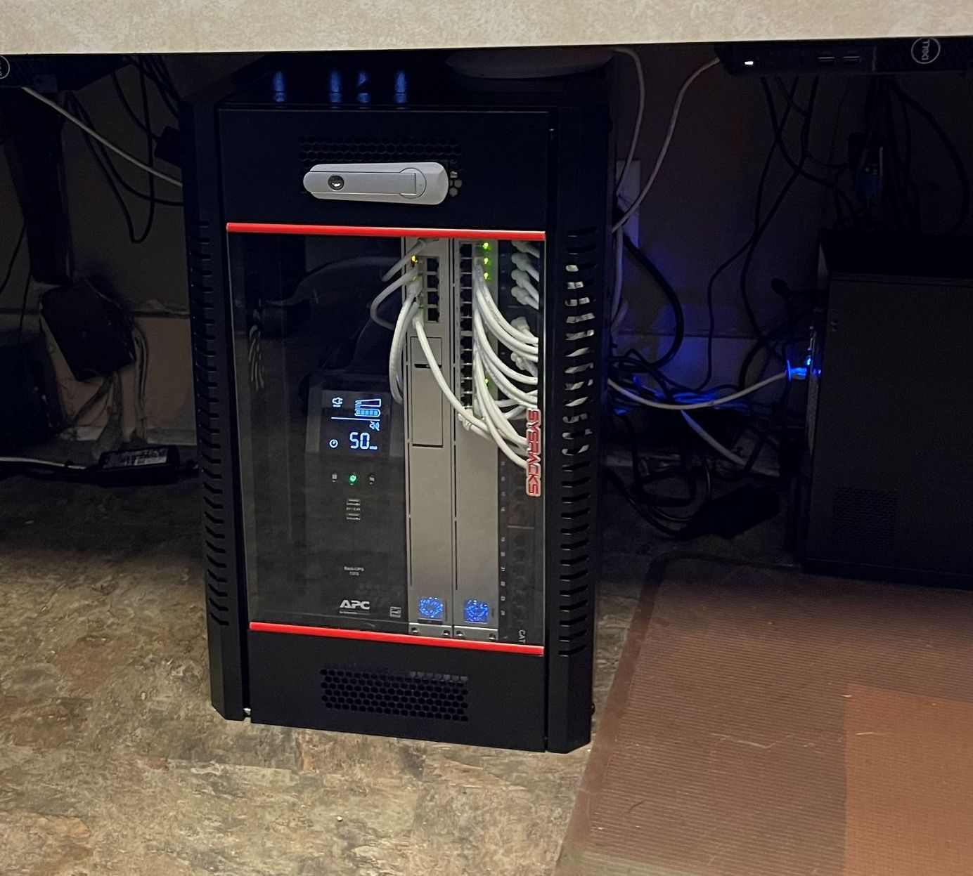A computer is sitting under a desk and has a clock on it